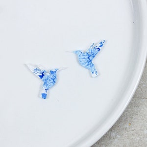 May include: Two blue and white hummingbird paper cutouts on a white plate.