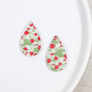 May include: Two clear teardrop-shaped acrylic charms with a strawberry and flower pattern.
