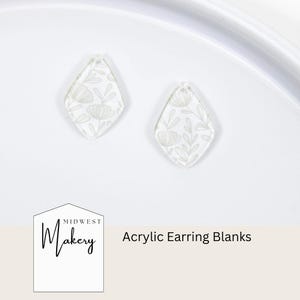 May include: Two clear acrylic earring blanks with a floral design. The blanks are diamond-shaped with a small hole at the top for attaching to earring hooks. The floral design is in a light beige color. The text "Acrylic Earring Blanks" is visible.