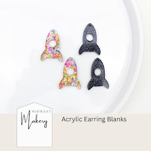 May include: Four acrylic earring blanks in a rocket ship design. Two rockets have a colorful floral pattern, and two are black with glitter. The text "Midwest Makery" and "Acrylic Earring Blanks" are also visible.