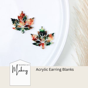 Puede incluir: Dos pares de pendientes de hoja de arce de acrílico con un diseño similar a la acuarela en tonos rojos, verdes y amarillos. Los blancos están sobre una superficie blanca. Midwest Makery Blancos de pendientes de acrílico.