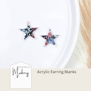May include: Two star-shaped acrylic earring blanks with a red, white, and blue firework pattern. The blanks are on a white plate. The text "Midwest Makery Acrylic Earring Blanks" is below the plate.