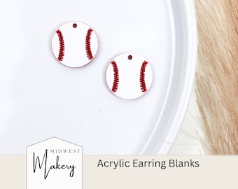 May include: Two white acrylic earring blanks shaped like baseballs with red stitching. The blanks are on a white plate. The text "Midwest Makery" and "Acrylic Earring Blanks" are visible below the plate.