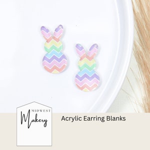 May include: Two pastel rainbow chevron patterned bunny shaped acrylic earring blanks. The blanks are on a white surface. The text "Midwest Makery Acrylic Earring Blanks" is at the bottom of the image.