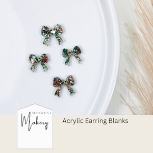 May include: Four red and green glitter bow earring blanks on a white surface. The text "Midwest Makery" and "Acrylic Earring Blanks" is visible below the bows.