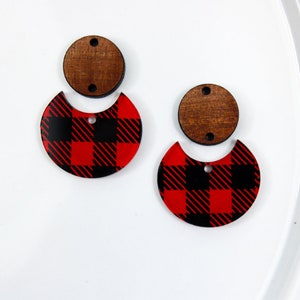 May include: A pair of earrings with a red and black buffalo plaid design. The earrings are made of wood and acrylic.