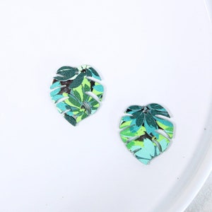 May include: Two green and blue tropical leaf shaped earrings with a white background.