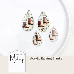 Può includere: Base per orecchini in acrilico a forma di goccia, con un design di stivali da cowboy marroni su sfondo floreale. Gli orecchini sono esposti su un piatto bianco. Il testo "Acrylic Earring Blanks" è visibile.