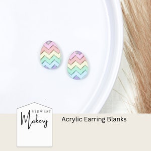 May include: Two pastel rainbow chevron patterned acrylic earring blanks. The blanks are shaped like an egg and have a hole at the top for attaching earring hooks. The blanks are on a white surface.