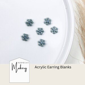 May include: Six blue glitter snowflake acrylic earring blanks on a white plate.  Midwest Makery Acrylic Earring Blanks.