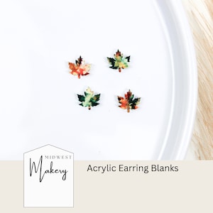 Puede incluir: Cuatro piezas en blanco para pendientes de acrílico con forma de hojas de arce con un estampado de follaje otoñal. Las hojas son en tonos de verde, naranja y rojo. El texto "Midwest Makery Acrylic Earring Blanks" está en la parte inferior de la imagen.