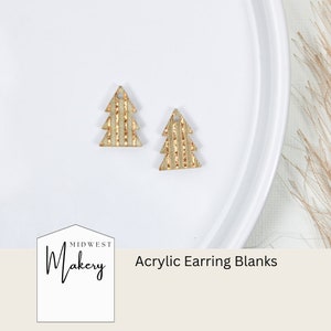 May include: Two gold acrylic Christmas tree earring blanks on a white plate. The plate is on a beige surface. The text "Midwest Makery" and "Acrylic Earring Blanks" is visible in the image.