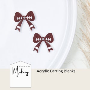 May include: Two maroon acrylic earring blanks shaped like footballs with white stitching details. The earring blanks are in a bow shape. The text "Acrylic Earring Blanks" is visible in the image.