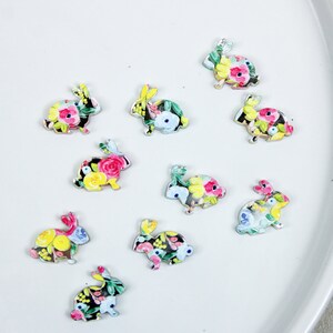 May include: Ten floral patterned wooden bunny shapes. The bunnies are painted in shades of pink, yellow, green, and blue. The bunnies are all facing the right side of the image.