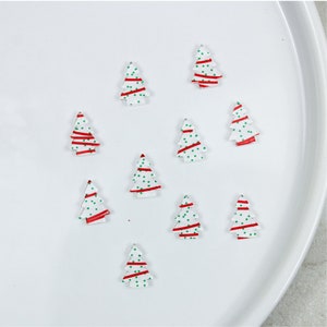 K&ouml;nnte beinhalten: Zehn wei&szlig;e Weihnachtsbaumschmuckst&uuml;cke mit roten und gr&uuml;nen Designs. Die Schmuckst&uuml;cke sind in einem Kreis auf einer wei&szlig;en Oberfl&auml;che angeordnet.