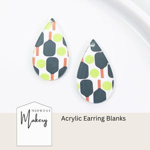 May include: Two teardrop-shaped acrylic earring blanks featuring a repeating pattern of dark gray pickleball paddles with orange handles and bright yellow pickleballs on a white background. Each piece has a small hole at the top for hanging.