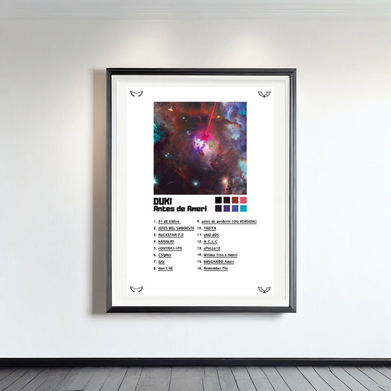 Op de afbeelding: Een ingelijste poster met de Duki Antes de Ameri albumhoes, een ruimte-nevelafbeelding, een kleurenpalet van zes vierkanten en een tracklist van zestien nummers. Het ontwerp staat op een witte achtergrond met kleine zwarte vleugeliconen.