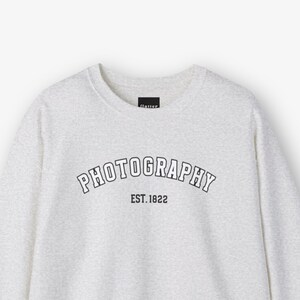 May include: A heather gray sweatshirt with the text "PHOTOGRAPHY EST. 1822" in a black arch.