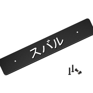 May include: A black carbon fibre license plate with the Japanese characters for "Subaru" in white. The plate has two mounting holes and is accompanied by several black screws.