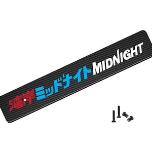 May include: Black carbon fiber license plate frame with white text that reads "MIDNIGHT" and Japanese text in blue and red. The frame comes with two black screws.