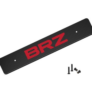 May include: Black carbon fiber license plate frame with red "BRZ" lettering. The frame comes with mounting hardware.
