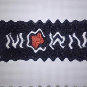 Pode incluir: Patch bordado em preto e branco com um coração vermelho no centro. O patch tem uma borda ondulada e diz "MORRI" em letras brancas.