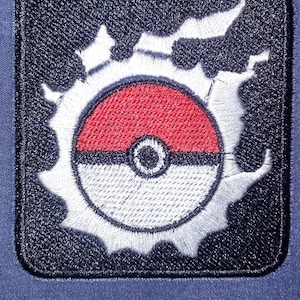 May include: A black and white embroidered patch with a red, white, and black Pokeball design. The Pokeball is surrounded by a white, jagged, star-shaped design.