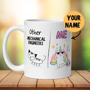 Puede incluir: Taza de cerámica blanca con un contorno negro de un gato en el lado izquierdo y un gato unicornio en el lado derecho. El texto "Other Mechanical Engineers" está en el lado izquierdo y "ME" está en el lado derecho. El texto "YOUR NAME" está en un círculo amarillo.