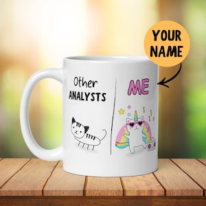 以下が含まれることがあります： 白磁のコーヒーカップ。左側に猫、右側にユニコーンの猫の白黒イラストが描かれている。猫のイラストの上に「Other Analysts」、ユニコーンの猫のイラストの上に「ME」と書いてある。黄色い円の中に「YOUR NAME」と書いてある。