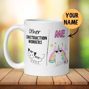 May include: White ceramic mug with a handle featuring a humorous design. The mug is divided into two sections: "Other Construction Workers" with a cat illustration, and "ME" with a cat unicorn wearing sunglasses, a rainbow, and a boombox. The text "YOUR NAME" is also present.
