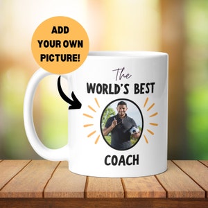 May include: White ceramic coffee mug with a black and yellow design. The mug says "The World's Best Coach" with a photo frame in the centre. The text "Add Your Own Picture!" is in a yellow circle.