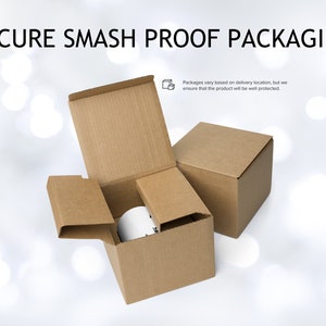 May include: Two brown cardboard boxes, one inside the other, with the top box open. The inner box contains a white mug. The text "SECURE SMASH PROOF PACKAGING" is at the top of the image. The text "Packages vary based on delivery location, but we ensure that the product will be well protected." is at the bottom of the image.