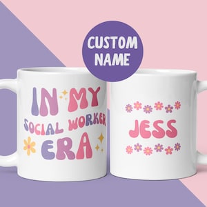 Könnte beinhalten: Eine weiße Keramiktasse mit einem rosa, violetten und gelben Design. Die Tasse trägt den Schriftzug "In My Social Worker Era" mit einer Blume und Sternen. Die andere Seite der Tasse hat ein rosa und violettes Blumendesign und den Namen "Jess".