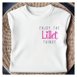 Könnte beinhalten: Weißes T-Shirt mit dem Text "Enjoy the Little Things" in schwarzer Schrift und "Little" in rosa Schrift mit einem kleinen Herz.
