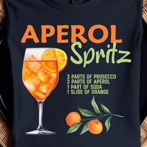 Könnte beinhalten: Ein marineblaues T-Shirt mit dem Text "APEROL Spritz" in orangefarbenen und grünen Buchstaben. Ein Glas Aperol Spritz ist mit einer Orangenscheibe abgebildet. Das Rezept für das Getränk ist unter dem Bild aufgeführt: 3 Teile Prosecco, 2 Teile Aperol, 1 Teil Soda, 1 Scheibe Orange.