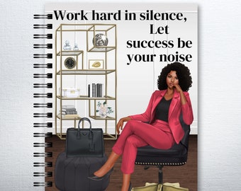 May include: A motivational quote, "Work hard in silence, Let success be your noise", is displayed on a pink and black notebook with a woman in a pink suit sitting in a chair. The woman has dark skin and dark hair.