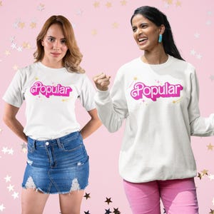 May include: Two people wearing white shirts with the word "Popular" printed in pink letters. The shirts have a sparkly design. One person is wearing a t-shirt and the other is wearing a sweatshirt.