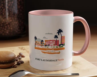 Puede incluir: Taza de cerámica blanca con borde y asa de color rosa. La taza presenta una ilustración colorida de una ciudad con palmeras y un barco en el agua. El texto "FORT LAUDERDALE Florida" está impreso en la parte inferior de la taza.