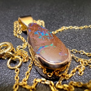 May include: A gold chain necklace with a teardrop-shaped pendant featuring a brown opal with blue and green flashes.
