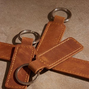 May include: Four brown leather keychains with silver key rings. The keychains are rectangular and have a stitched edge.