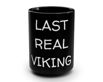 Puede incluir: Taza de cerámica negra con las palabras "LAST REAL VIKING" en blanco, en negrita y mayúsculas. La taza es cilíndrica y parece estar vacía.