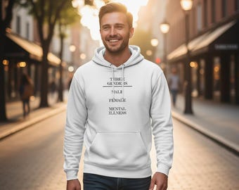May include: A white hooded sweatshirt with the text "THREE GENDERS IS MALE FEMALE MENTAL ILLNESS" in black. The person is wearing blue jeans and walking down a city street.