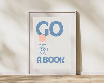 May include: A white framed poster with the text "GO GET LOST IN A BOOK" in blue lettering. The "GO" is in large, bold letters with a pink circle above the "O".