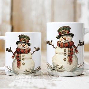 May include: Two white ceramic mugs with snowman designs. The larger mug features a snowman wearing a red and green plaid scarf and hat. The smaller mug features a similar snowman design.