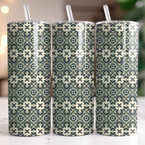 Può includere: Tre bicchieri in acciaio inossidabile con coperchi e cannucce. I bicchieri presentano un motivo ripetuto di forme floreali e geometriche verde scuro e color crema. I bicchieri sono cilindrici e sono esposti su una superficie bianca.