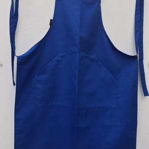 May include: A royal blue apron with a single large pocket in the front. The apron has adjustable straps that tie at the neck and waist.