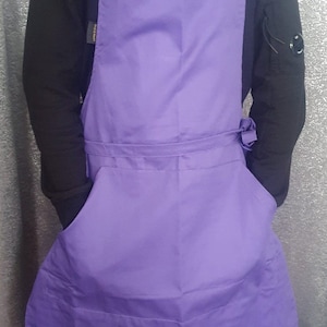 May include: A purple apron with adjustable straps and a large pocket. The apron is made from a durable, easy-to-clean fabric.