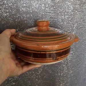 May include: A brown ceramic pot with a lid, featuring green and brown stripes. The pot has two small handles on the sides.