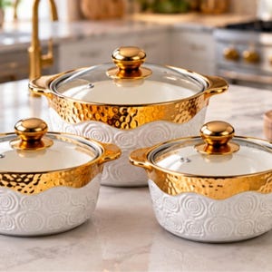 Könnte beinhalten: Ein Set aus drei weißen Keramik-Kochtöpfen mit geprägtem Rosenmuster und goldfarbenen, gehämmerten Metallrändern. Jeder Topf verfügt über zwei Seitengriffe und einen klaren Glasdeckel mit einem passenden goldfarbenen Knauf.