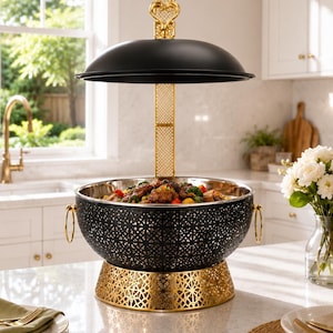Peut inclure: Un plat de service noir et doré avec un motif floral décoratif. Le plat a un couvercle en forme de dôme et est soutenu par un support doré. Le plat est rempli de nourriture et se trouve sur un comptoir de cuisine.